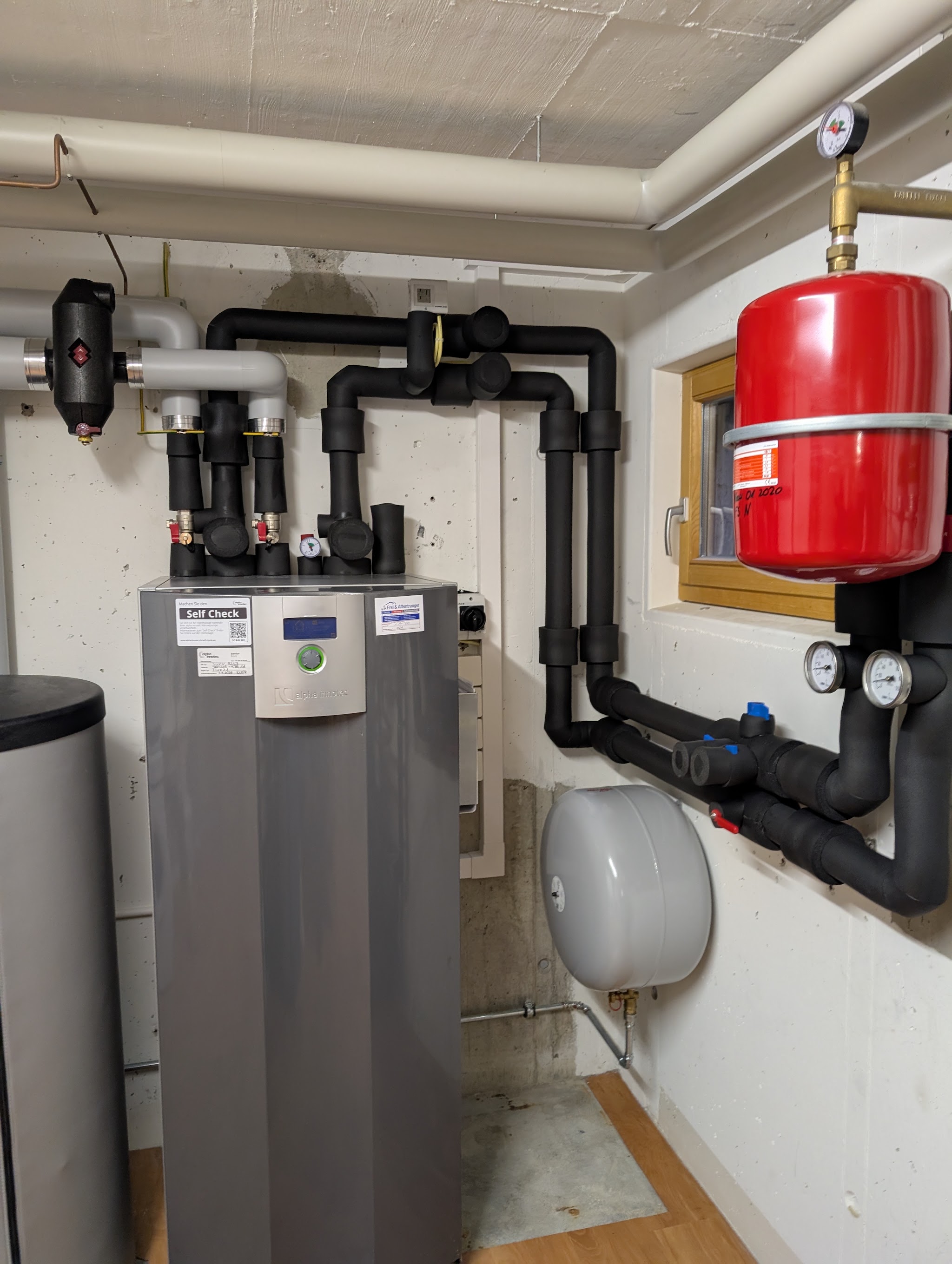 Wärmepumpe mit schwarz isolierten Rohren und rotem Ausdehnungsgefäss