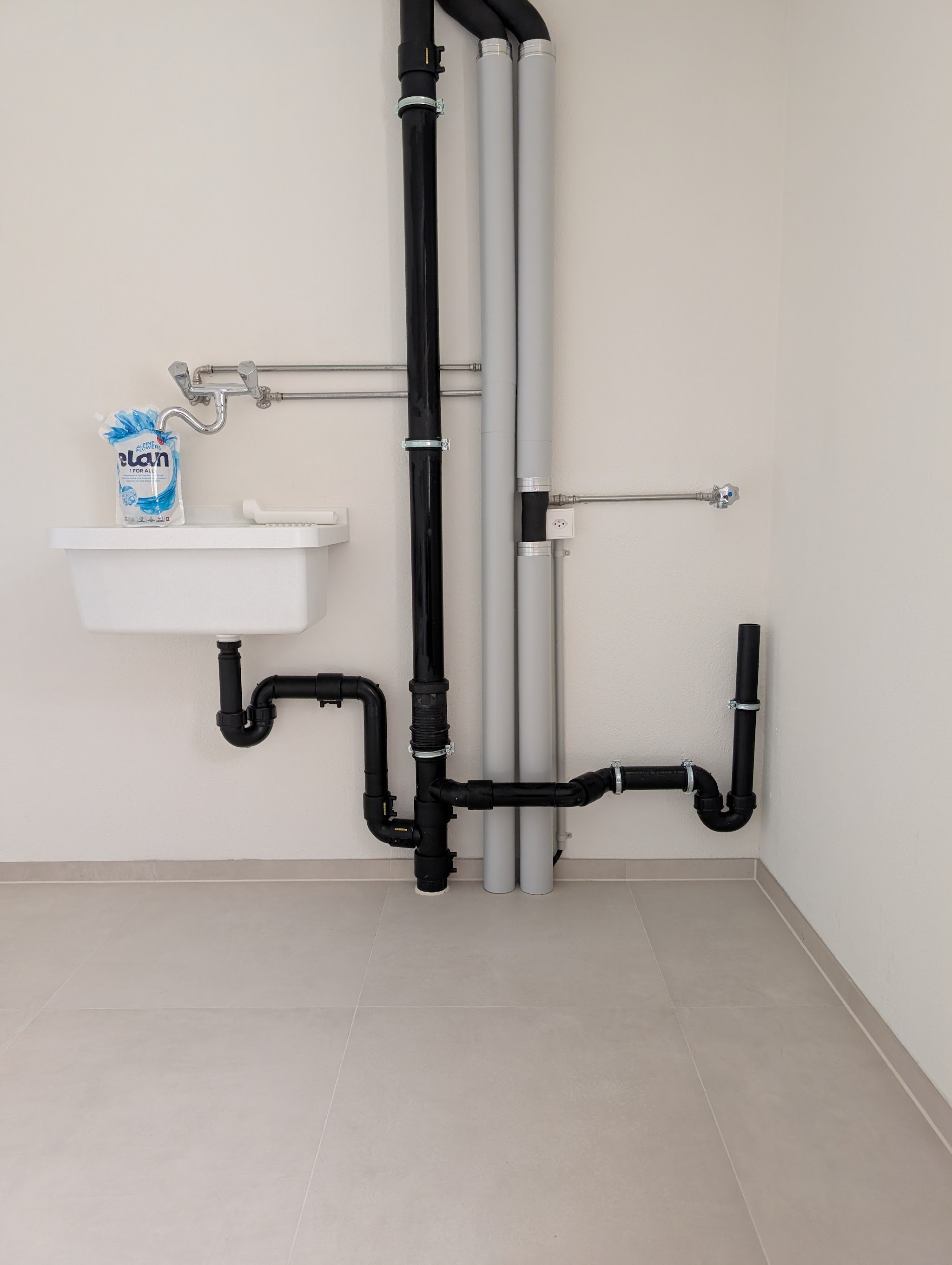 Isolierte Abwasser- und Heizungsleitungen an der Wand eines Waschraums