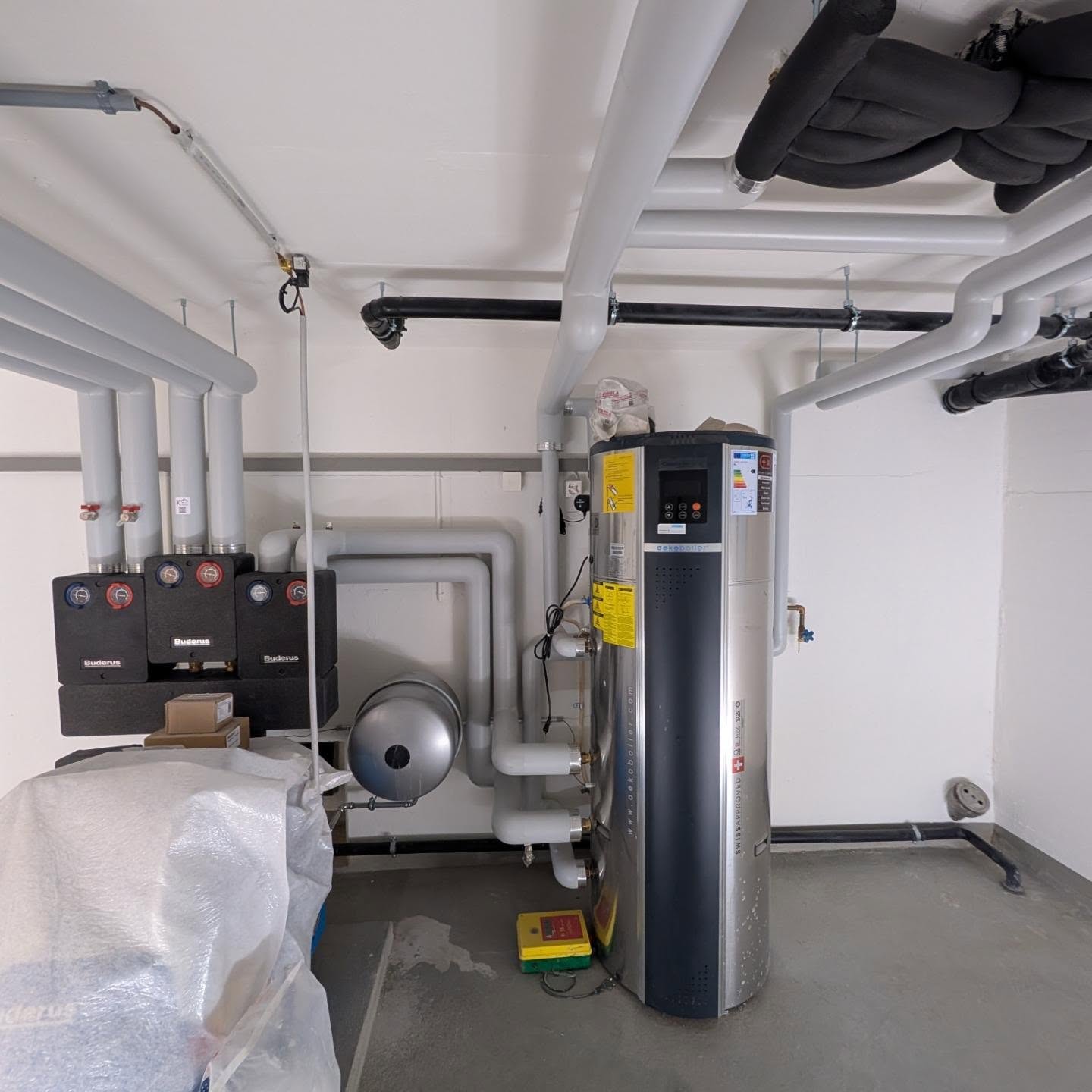 Technikraum mit Boiler, weiss isolierten Leitungen und Wärmepumpe